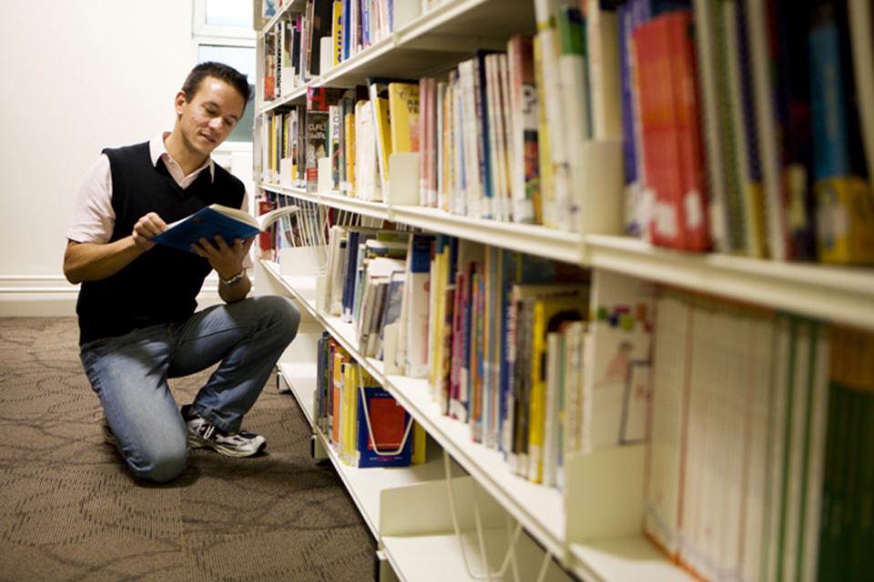 Young Man Reading a Book in a Library Book Shelf