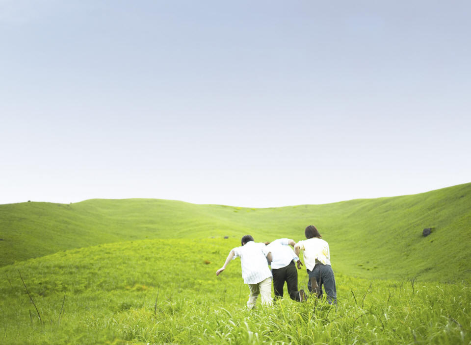 Three People Running through a large field of green grass